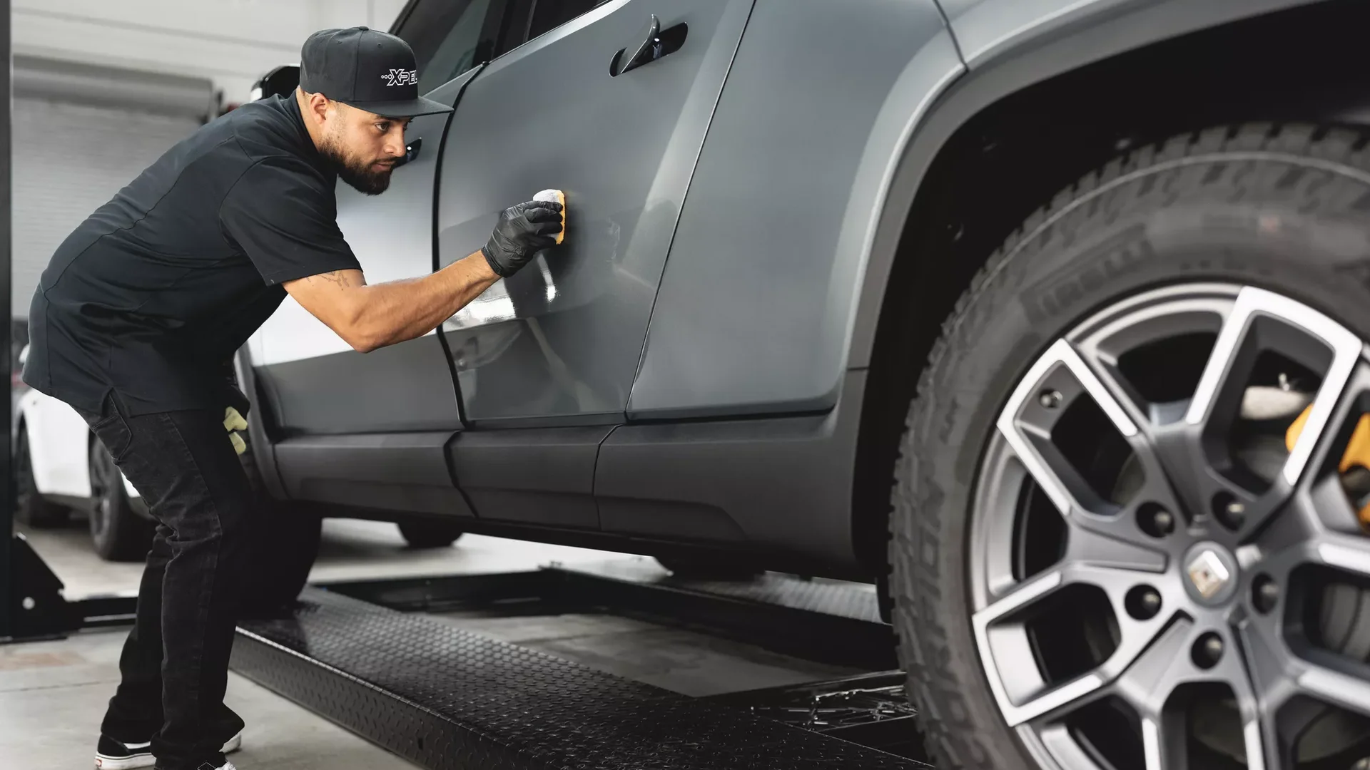 An XPEL technician applying ceramic coating to a grey SUV