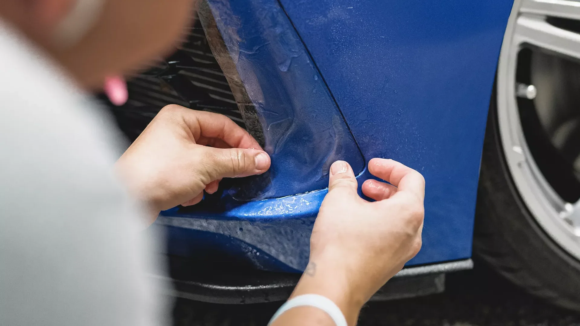 A technician carefully fitting XPEL paint protection film to a blue vehicle